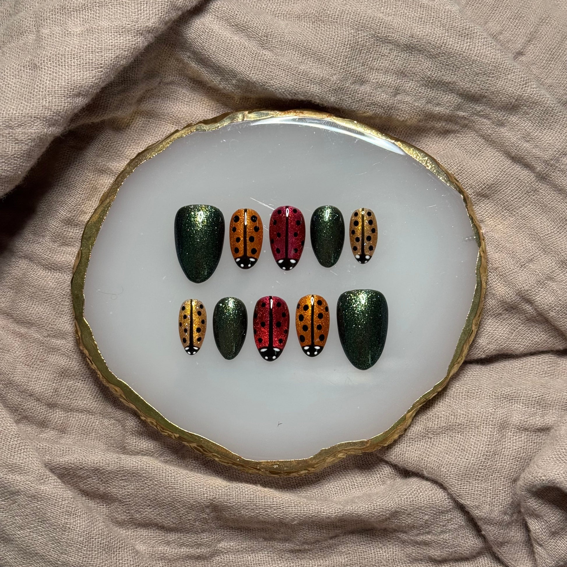 handmade sparkly gold, orange and red press on nails with lady bug designs and deep green accent nails, reusable, custom handmade press on nails, easy at-home manicure