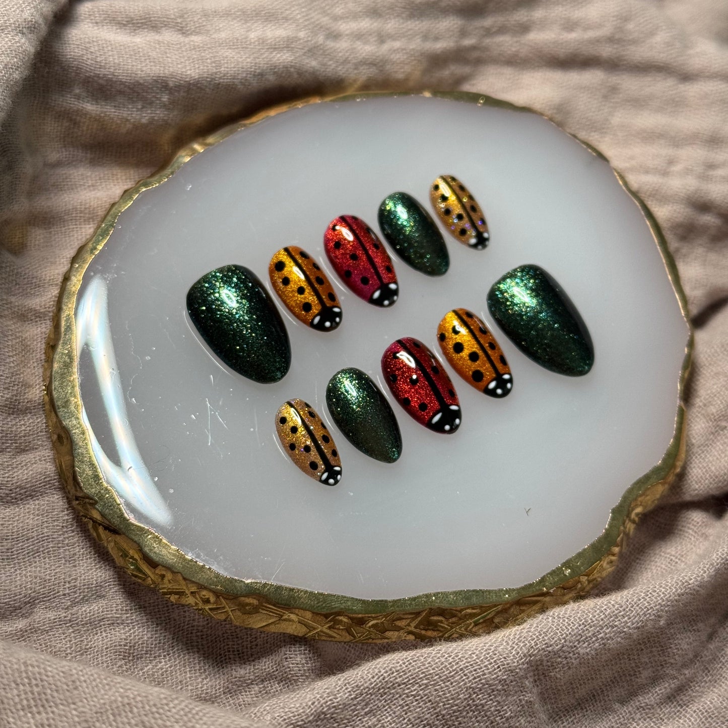 handmade sparkly gold, orange and red press on nails with lady bug designs and deep green accent nails, reusable, custom handmade press on nails, easy at-home manicure