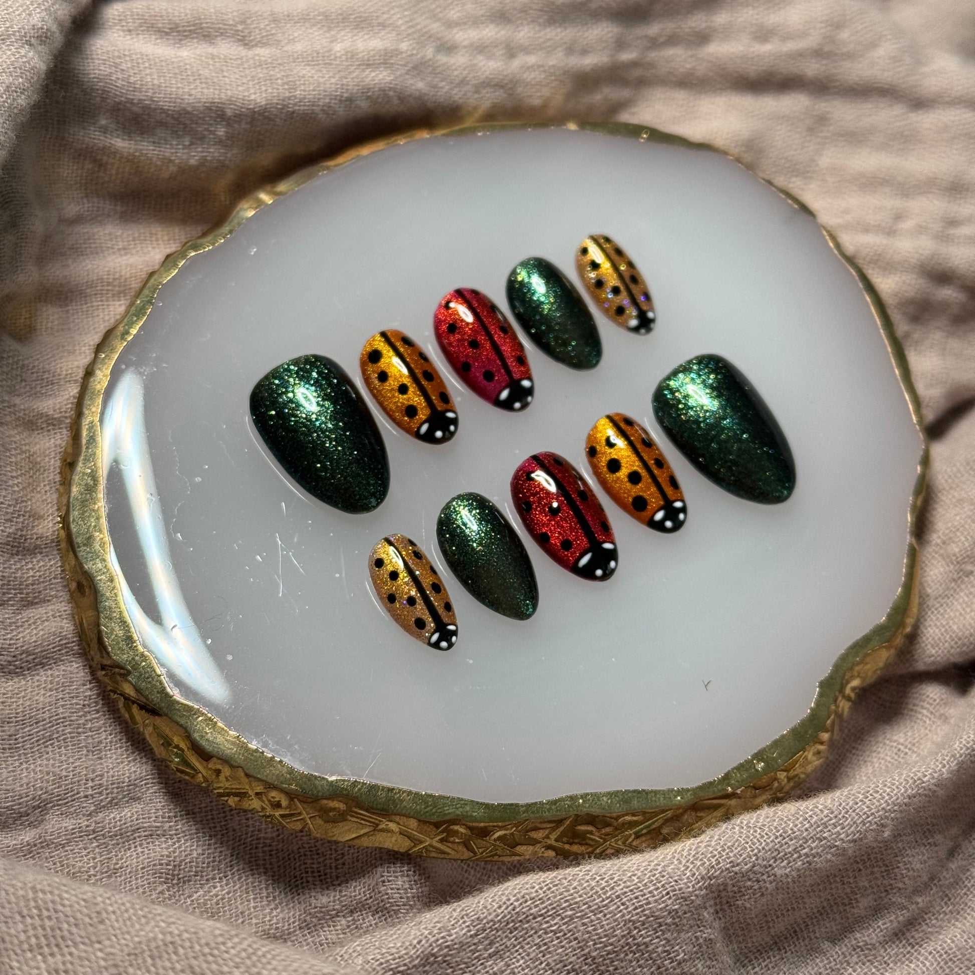 handmade sparkly gold, orange and red press on nails with lady bug designs and deep green accent nails, reusable, custom handmade press on nails, easy at-home manicure
